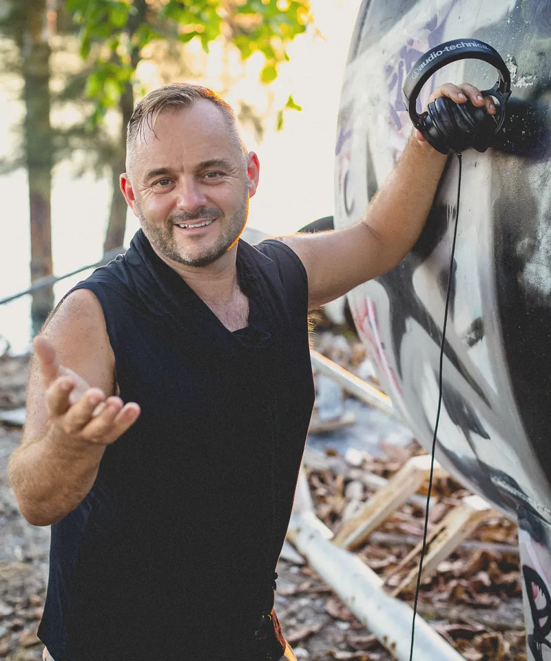 Portrait of Tristan Gorski smiling, one hand held out, headphones resting on a painted boat hull