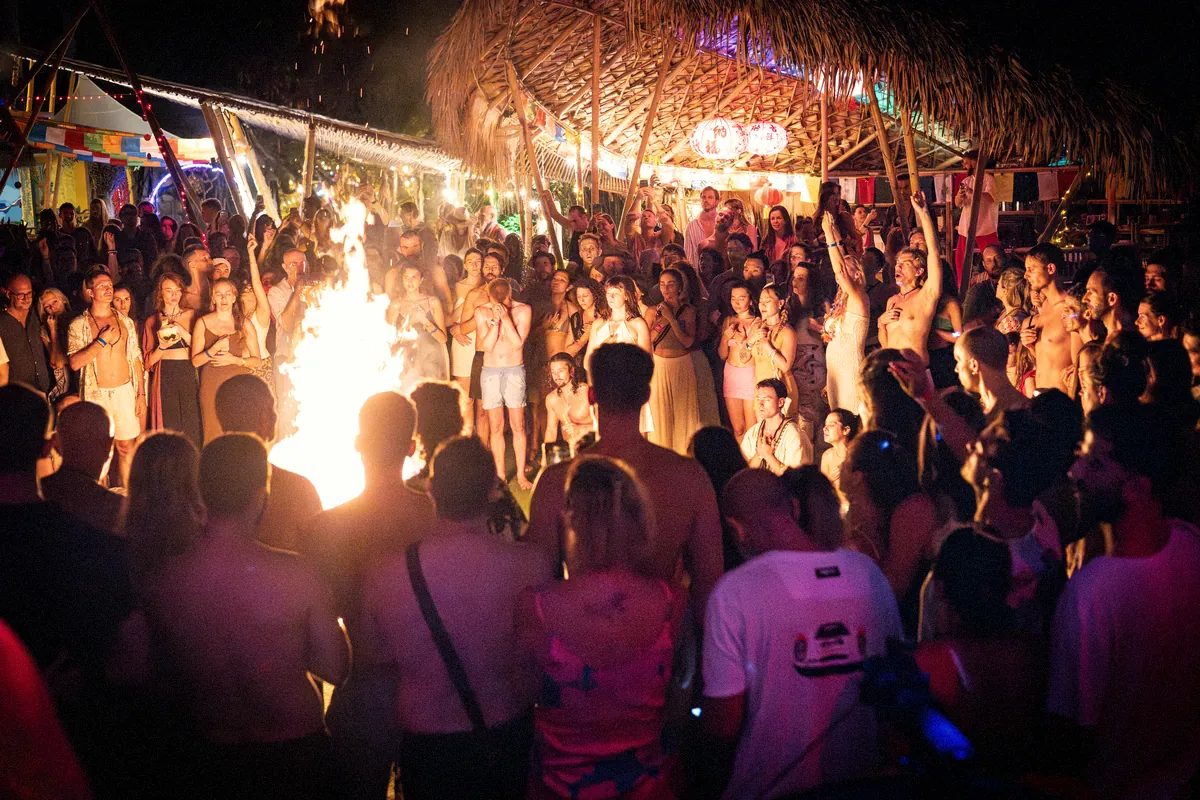 A crowd gathered around a bonfire under a bamboo roof at Ecstatica on New Year’s Eve