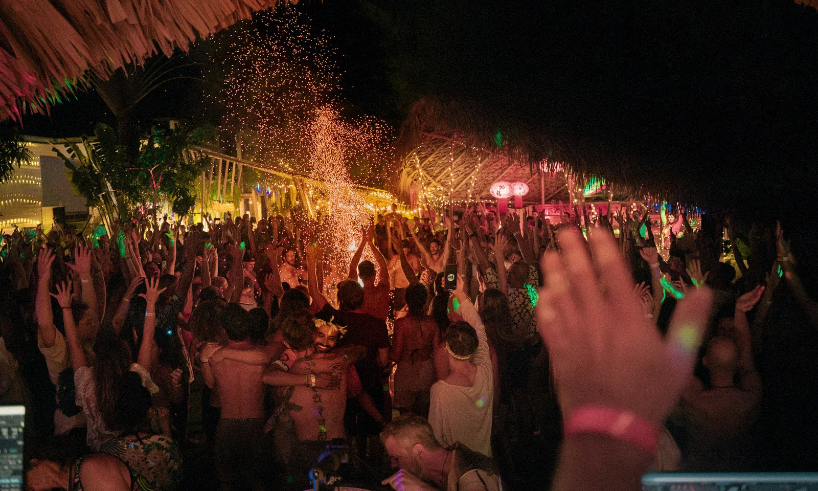A packed open-air dance floor on Koh Phangan at night, hands in the air and sparks rising