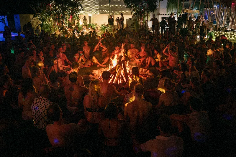 Hundreds of people sitting in a circle around a fire at night on Koh Phangan
