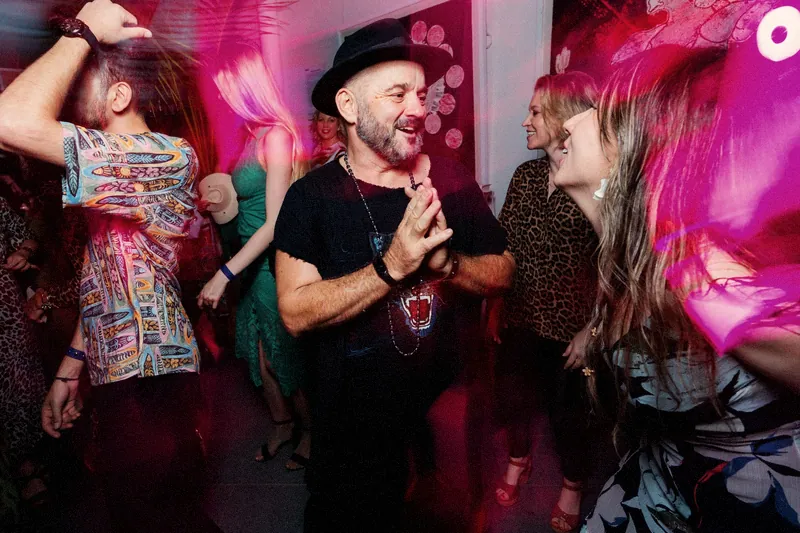 Tristan Gorski in a black hat, hands pressed together, smiling in the middle of a dance floor washed in pink light