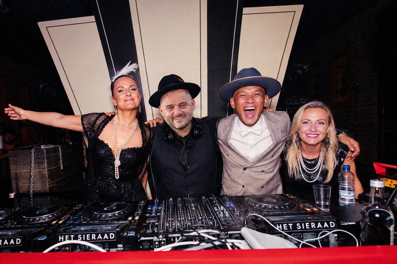 Tristan Gorski in a black hat with three friends behind the decks, arms around each other, laughing