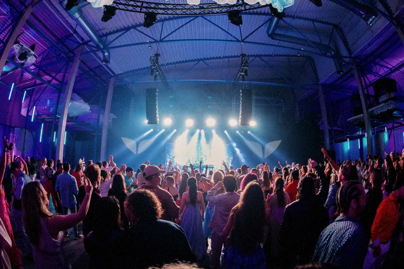A full hall of people dancing toward a brightly lit stage